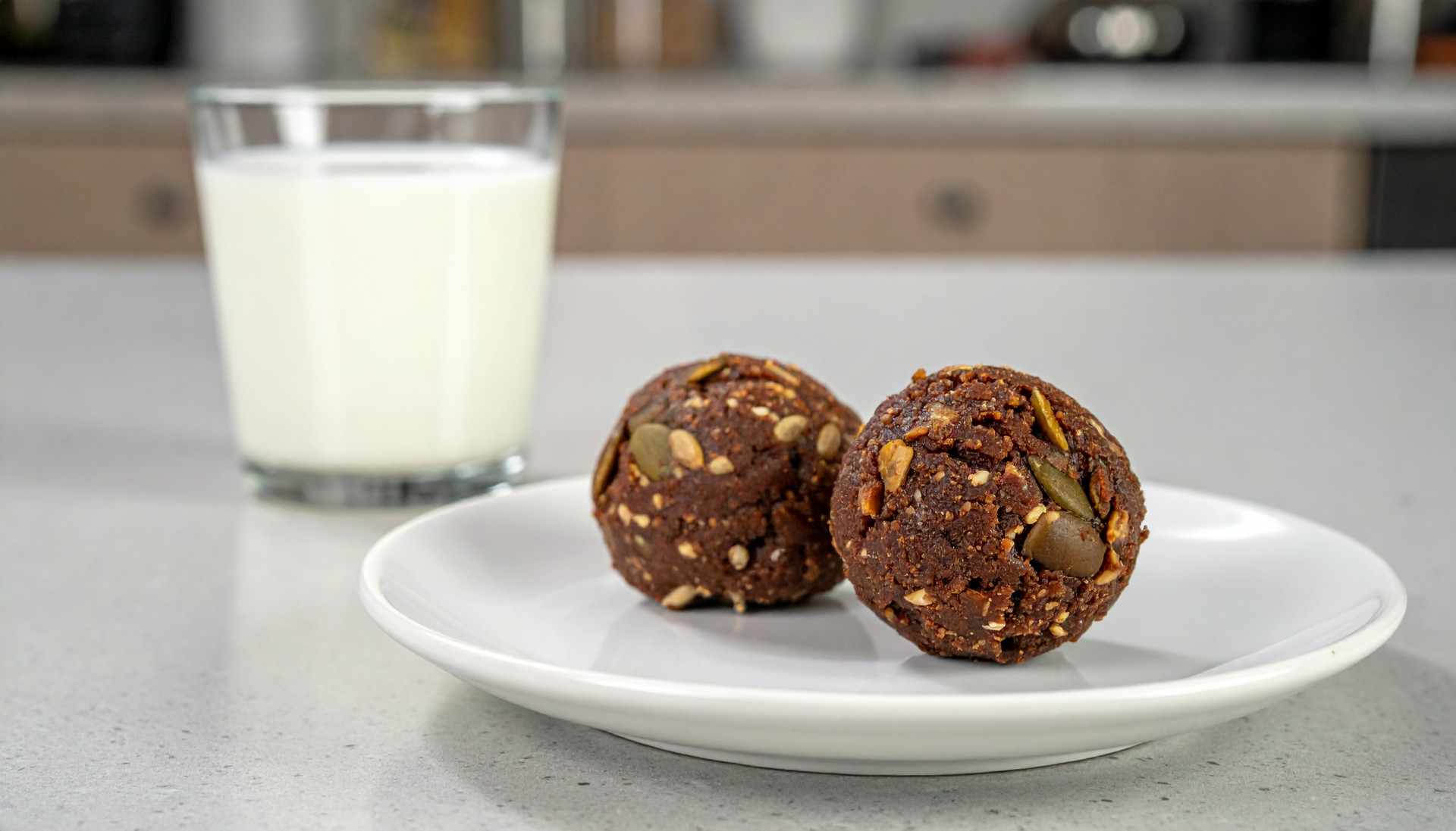 Two cocoa pumpkin seed bites with a glass of milk